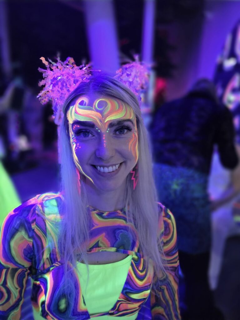 Rõõmsameelne uv-maalinguga tüdruk HAUX HAUX värvilise neoondžungli peol. UV-riietus, uv-tutid peas.