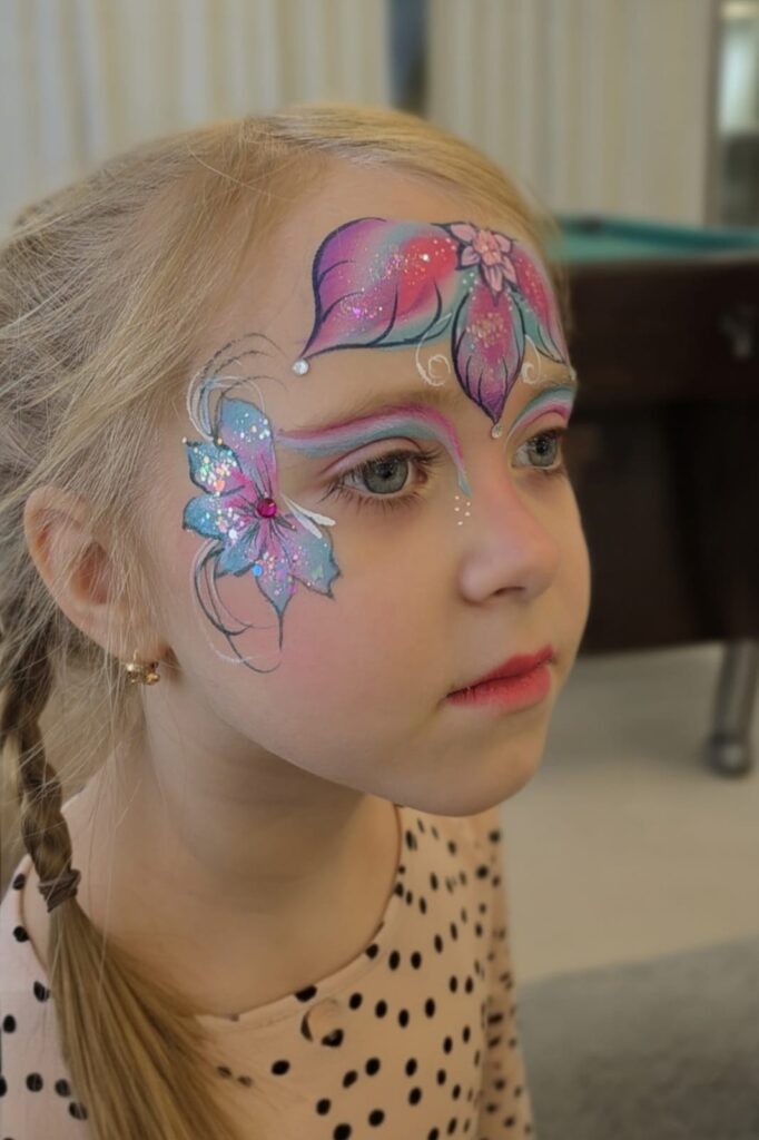 Tüdrukute näomaaling, helesinine ja roosa lill tüdruku näol, laste näomaaling, ornamentika, festivali glitter - Ilu loojad OÜ